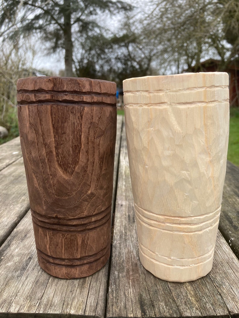 Puede incluir: Dos tazas de madera, una es marr&oacute;n y la otra es de madera clara. Ambas tazas tienen un dise&ntilde;o tallado alrededor del medio.