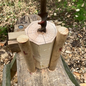 Puede incluir: Primer plano de una espiga de madera que se est&aacute; perforando con un taladro de mano. La espiga est&aacute; apoyada en un banco de trabajo de madera con otras dos espigas a cada lado. La espiga que se est&aacute; perforando tiene un c&iacute;rculo dibujado en ella con l&iacute;neas que irradian desde el centro.
