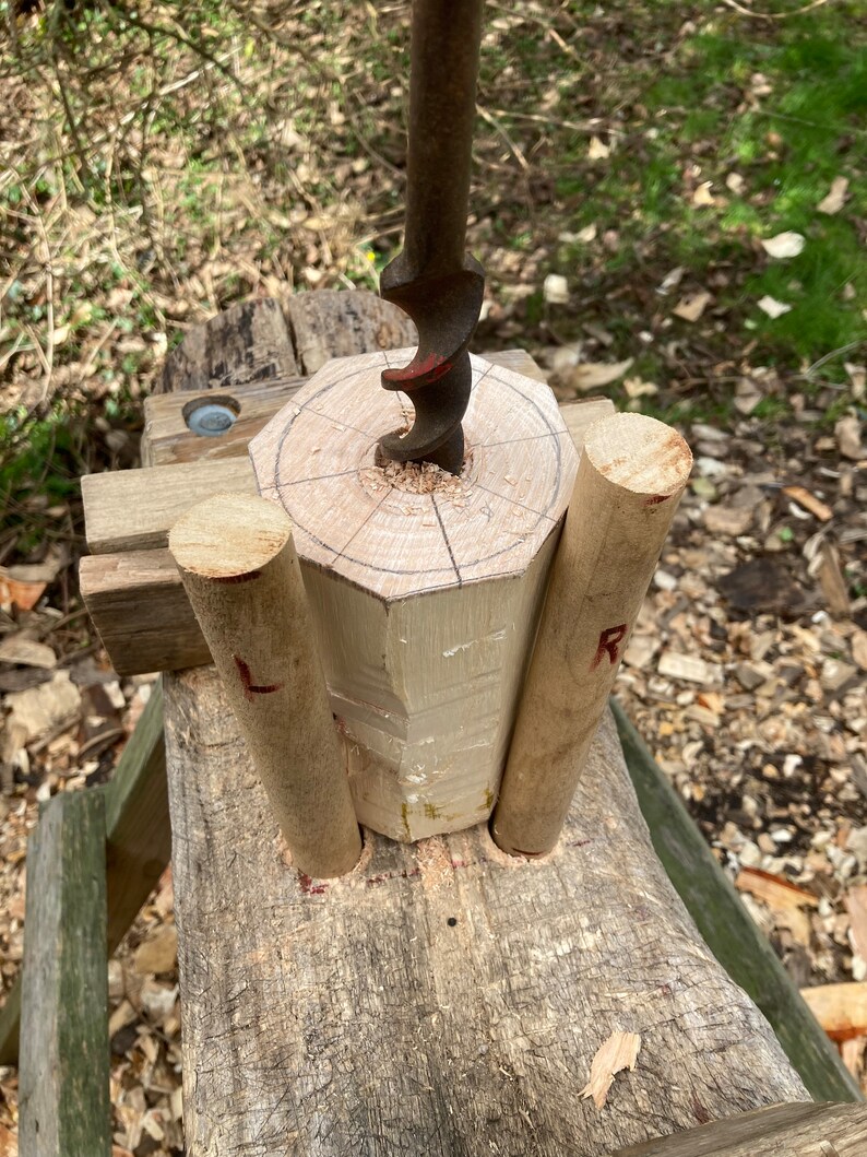 Puede incluir: Primer plano de una espiga de madera que se est&aacute; perforando con un taladro de mano. La espiga est&aacute; apoyada en un banco de trabajo de madera con otras dos espigas a cada lado. La espiga que se est&aacute; perforando tiene un c&iacute;rculo dibujado en ella con l&iacute;neas que irradian desde el centro.