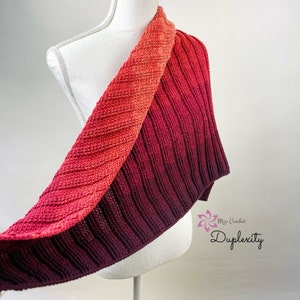 May include: A red and burgundy ombre crochet shawl with a textured stitch pattern. The shawl is draped over a white dress form.