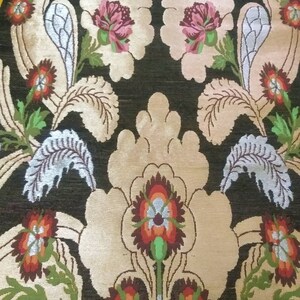 May include: A close-up of a fabric with a floral pattern. The fabric is black with beige, green, red, and white flowers. The flowers are stylized and have a vintage look.