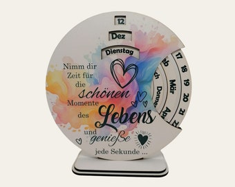 Könnte beinhalten: Ein hölzerner Perpetuum-Kalender mit einem bunten Aquarellhintergrund und dem Text "Nimm dir Zeit für die schönen Momente des Lebens und genieße jede Sekunde..." Der Kalender verfügt über ein drehbares Zifferblatt mit den Monaten Dezember, Februar, März und April.