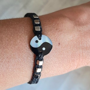 May include: A black and white yin yang charm bracelet with silver beads. The bracelet is made of black cord and has a silver clasp.