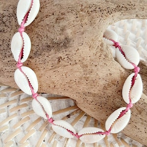 May include: A pink string bracelet with white seashells. The bracelet is tied in a knot and is ready to be worn.