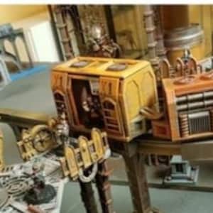 May include: A model of a sci-fi vehicle in yellow and brown colours. The vehicle has a raised platform with a ladder and a small figure inside. The vehicle is on a track and has the number "1" on the side.