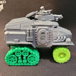 May include: A grey plastic model of a tracked armoured vehicle with a green track and a green wheel. The vehicle has a raised turret with a gun and a figure on top.
