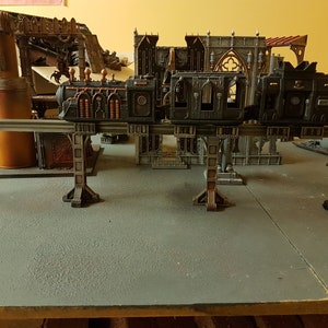 May include: A model train set with two carriages on a raised track. The train is black with silver accents and is made of plastic. The track is made of metal and is supported by four metal pillars. The train is on a grey surface.