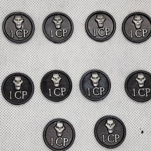 Peut inclure: Dix jetons ronds noirs et argentés avec un motif de crâne et le texte "1 CP" sur chacun.