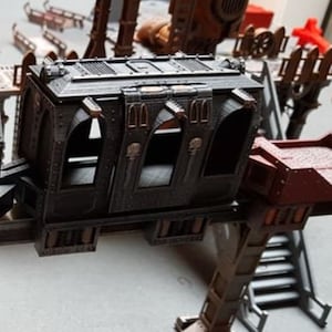 May include: A black metal model train carriage with three windows and a detailed design. The carriage is attached to a metal structure with a staircase.