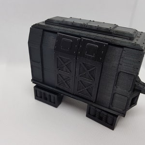 May include: A black, 3D printed model of a train carriage with a detailed exterior and a hinged door. The carriage has a flat roof with a raised section in the centre. The carriage is sitting on a white surface.