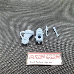 May include: A set of four 3D printed light blue plastic parts for a model kit. The parts include a small cylinder with a hole in the side, a larger cylinder with a hole in the side, and two small rods.