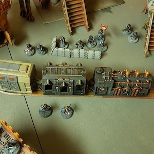 May include: A model train set featuring a beige boxcar, a black passenger car, and a black steam engine with copper piping. The train is on a brown track with a brown and gold metal base.