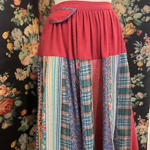 Könnte beinhalten: Ein Patchwork-Rock mit rotem Bund und einer Vielzahl gemusterter Stoffe im Rock. Der Rock hat eine rote Tasche mit blauem Besatz. Der untere Teil des Rocks enthält Karomuster, Blumenmuster und Streifen.