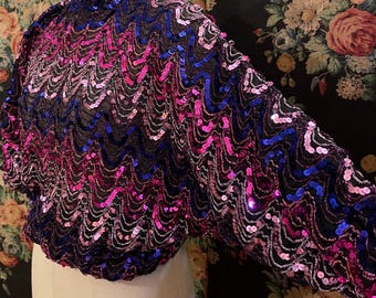 May include: A sequined top with a high neck and long sleeves. The top is made of a black mesh fabric with pink, blue, and silver sequins. The sequins are arranged in a wavy pattern.