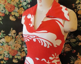 May include: A sleeveless dress featuring a vibrant red and white abstract floral pattern. The garment has a pointed collar and a deep V-neckline, displayed on a mannequin. The fabric displays a bold, high-contrast design with organic shapes.