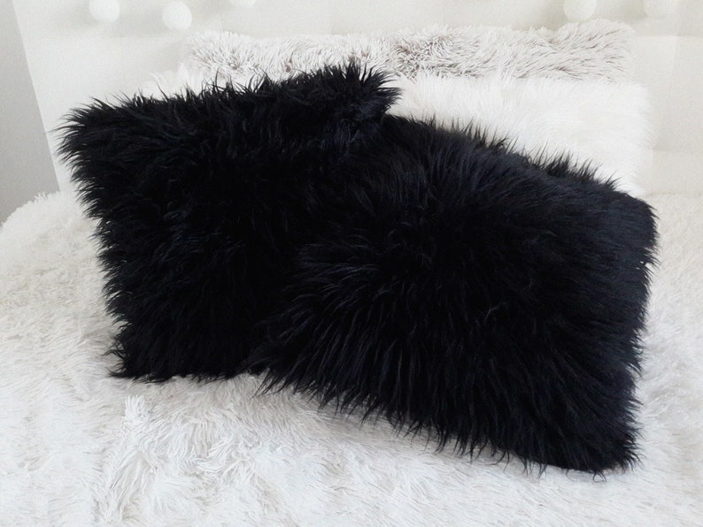 Puede incluir: Dos almohadas mullidas negras sobre una superficie mullida blanca. Las almohadas est&aacute;n hechas de un material suave y mullido.