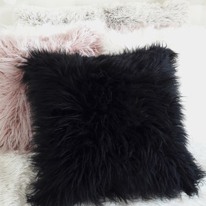 Puede incluir: Una almohada negra y esponjosa sobre una superficie blanca y esponjosa. La almohada es cuadrada y tiene una textura suave y mullida.