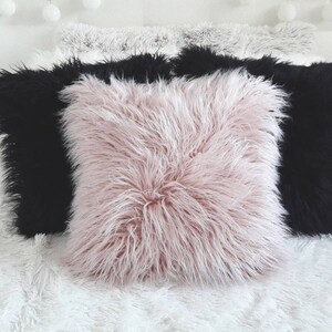 May include: Three decorative throw pillows with a fluffy texture. The pillows are in a white, black, and pink color scheme.