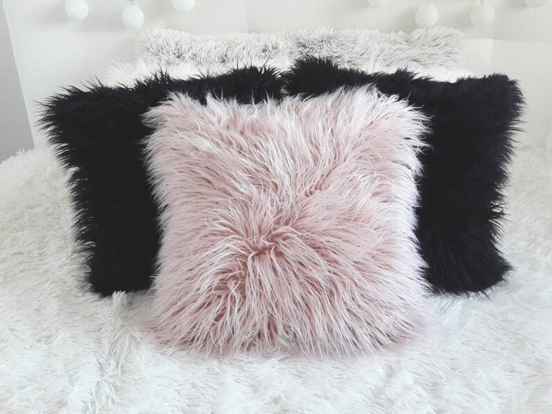 May include: Three decorative throw pillows with a fluffy texture. The pillows are in a white, black, and pink color scheme.