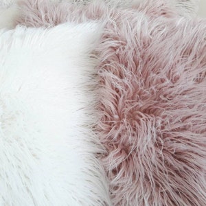 May include: Two fluffy throw pillows, one white and one light pink. The pillows are made of a soft, plush material and would be perfect for adding a touch of comfort and style to any room.