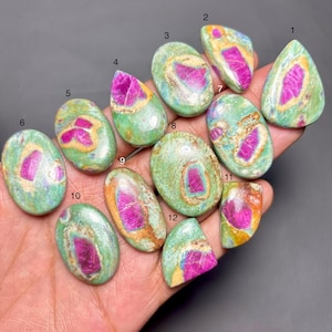 May include: A collection of polished gemstones with a vibrant color palette. Each stone features a striking combination of pink and green hues, with some displaying hints of yellow and orange. The stones vary in shape, from oval to teardrop.