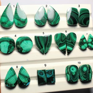 May include: A collection of ten pairs of polished malachite gemstones in various shapes, including teardrops, ovals, and hearts. The stones display a vibrant green color with distinctive swirling patterns.