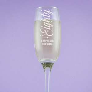 May include: A clear glass champagne flute with the text "Eighty Happy 80th Grandma" etched on the side.