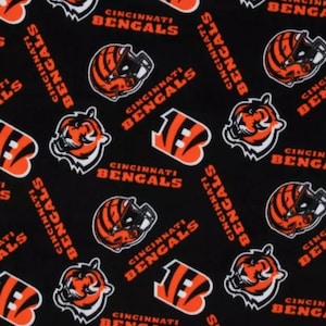 May include: Black fabric featuring a repeating pattern of Cincinnati Bengals logos, helmets, and text. The logos are orange, black, and white. The text reads "Cincinnati Bengals" in orange. This fabric is suitable for various crafting projects.