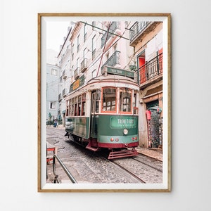 May include: A vintage green and white tram with the words "Tram Tour" on the side, travelling down a cobbled street in Lisbon, Portugal.