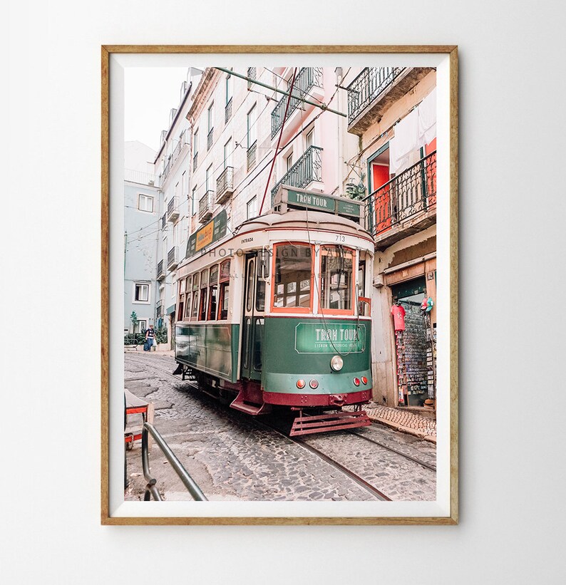 May include: A vintage green and white tram with the words "Tram Tour" on the side, travelling down a cobbled street in Lisbon, Portugal.