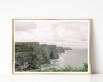 May include: A photograph of the Cliffs of Moher in Ireland. The cliffs are tall and rugged, with a green grassy top and a rocky base. The ocean is a deep blue, and the sky is a light blue with white clouds.