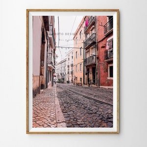 May include: A narrow cobbled street in a European city with colourful buildings on either side. The street is lined with tram tracks and there are clothes hanging on lines outside the windows.