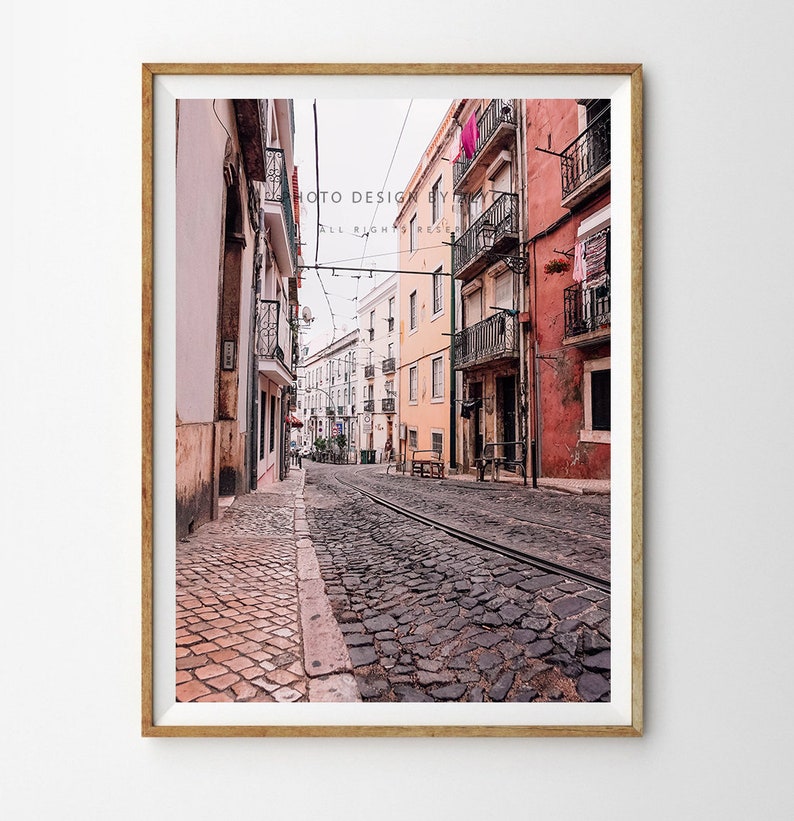 May include: A narrow cobbled street in a European city with colourful buildings on either side. The street is lined with tram tracks and there are clothes hanging on lines outside the windows.