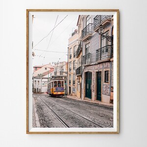 May include: A yellow and purple vintage tram travels down a cobbled street lined with colourful buildings in Lisbon, Portugal.