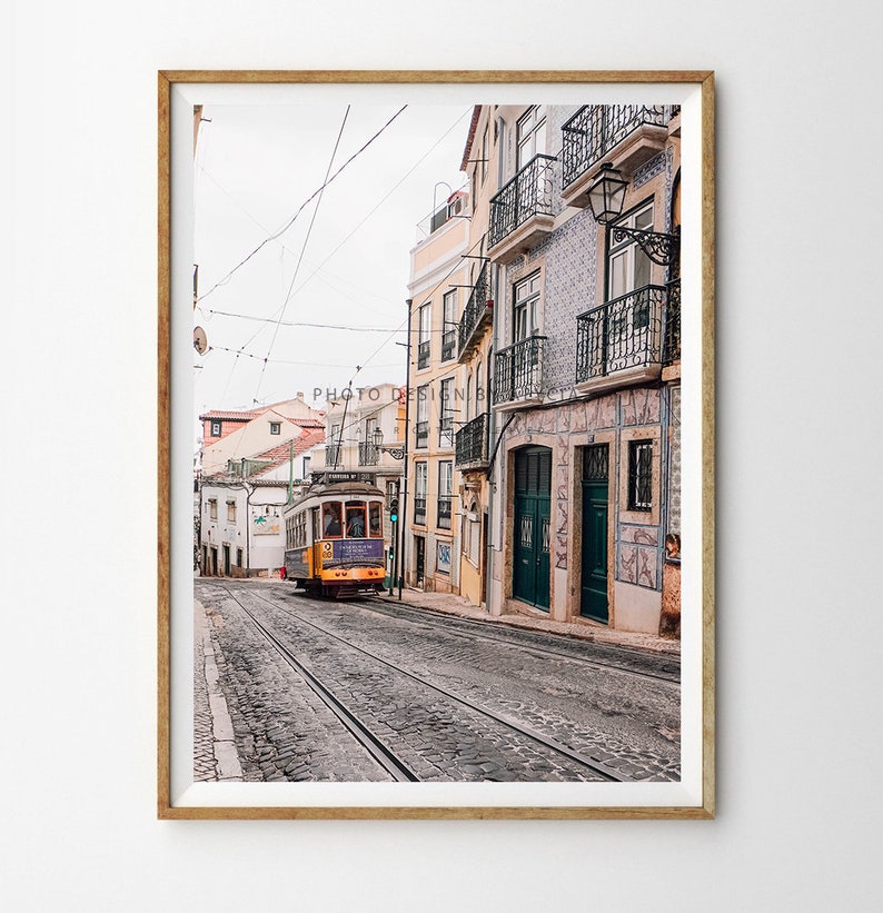 May include: A yellow and purple vintage tram travels down a cobbled street lined with colourful buildings in Lisbon, Portugal.