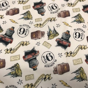 Op de afbeelding: Witte stof met een herhalend patroon van Harry Potter-thema illustraties. Het patroon bevat een rode stoomlocomotief, een koffer, een kasteel, een bliksem, sterren en de woorden "Platform 9 3/4".