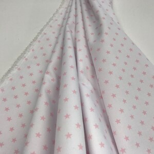 May include: White fabric with a pink star pattern. The fabric is folded and has a frayed edge.