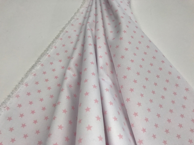 May include: White fabric with a pink star pattern. The fabric is folded and has a frayed edge.