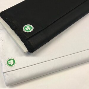 Puede incluir: Dos rollos de tela, uno blanco y otro negro, con una etiqueta de certificación Global Organic Textile Standard (GOTS) verde y blanca en cada uno.