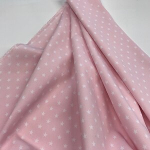 May include: Pink fabric with a white star pattern. The fabric has a corduroy texture.