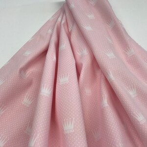 May include: Pink fabric with a white crown pattern. The fabric has a textured surface.