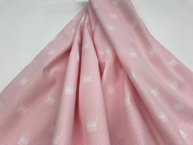 May include: Pink fabric with a white crown pattern. The fabric has a textured surface.