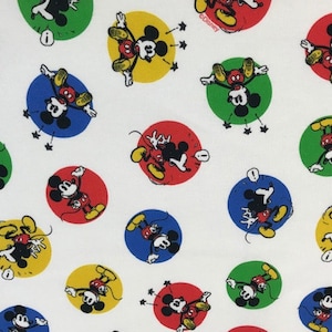 May include: White fabric with a repeating pattern of Mickey Mouse in different coloured circles. Mickey Mouse is depicted in a classic cartoon style with red shorts, yellow shoes, and white gloves. The circles are red, yellow, blue, and green.