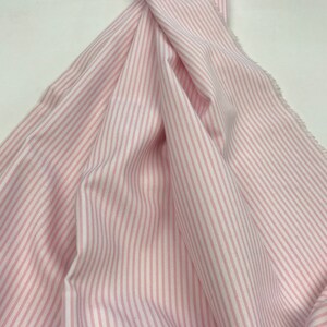 May include: Pink and white striped fabric with a subtle sheen. The fabric is folded and draped, showcasing the vertical stripes.