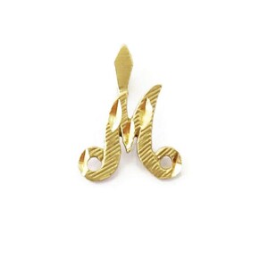 May include: A gold-colored pendant in the shape of the letter "M". The pendant has a textured surface and a pointed top.