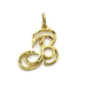 May include: A gold-colored pendant in the shape of the letter B. The letter is stylized with a decorative, swirling design.