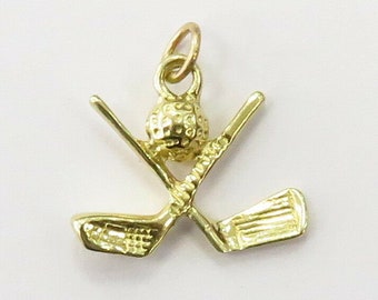 Könnte beinhalten: Ein goldfarbener Golfschläger-Anhänger mit einem Golfball oben drauf. Der Anhänger ist als Anhänger für eine Halskette oder ein Armband gedacht.