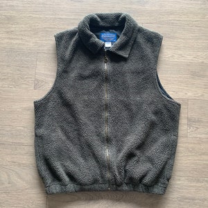 Puede incluir: Un chaleco de vellón gris oscuro con cierre de cremallera y cuello. El chaleco tiene una etiqueta de marca que dice "Pendleton".
