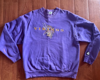 May include: Purple sweatshirt with a vintage embroidered Minnesota Vikings logo and the word "VIKINGS" in orange.