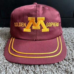 Könnte beinhalten: Eine marineblaue Baseballkappe mit einem goldenen, gestickten "M" und den Worten "Golden Gophers".